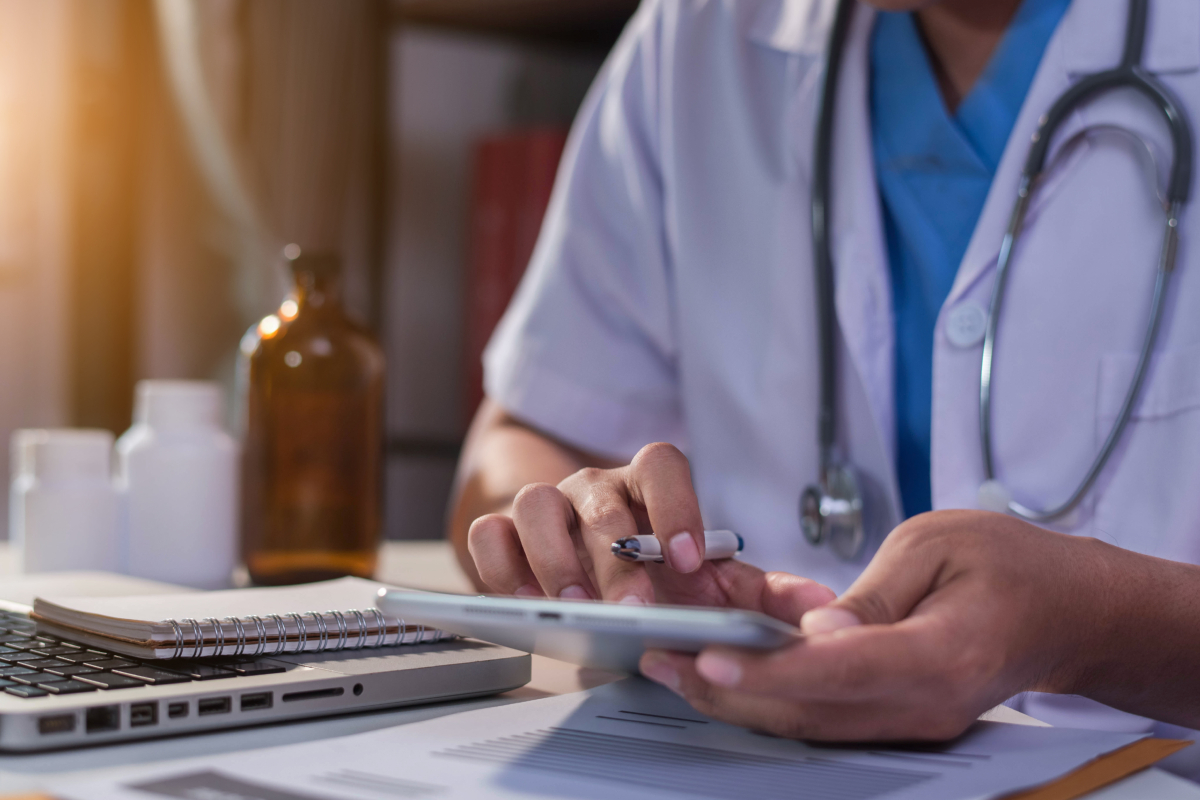 A healthcare professional using a smartphone next to a laptop.