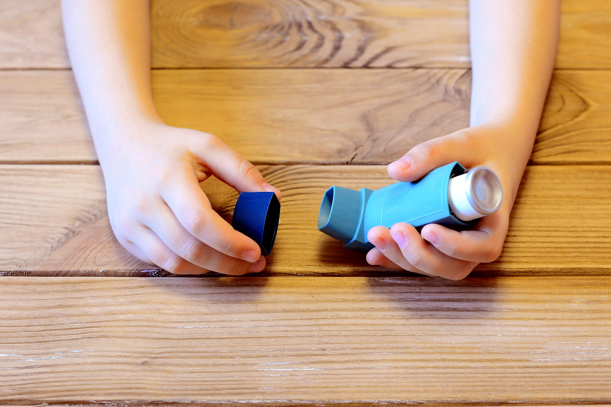 A child's hands holding a blue asthma inhaler.